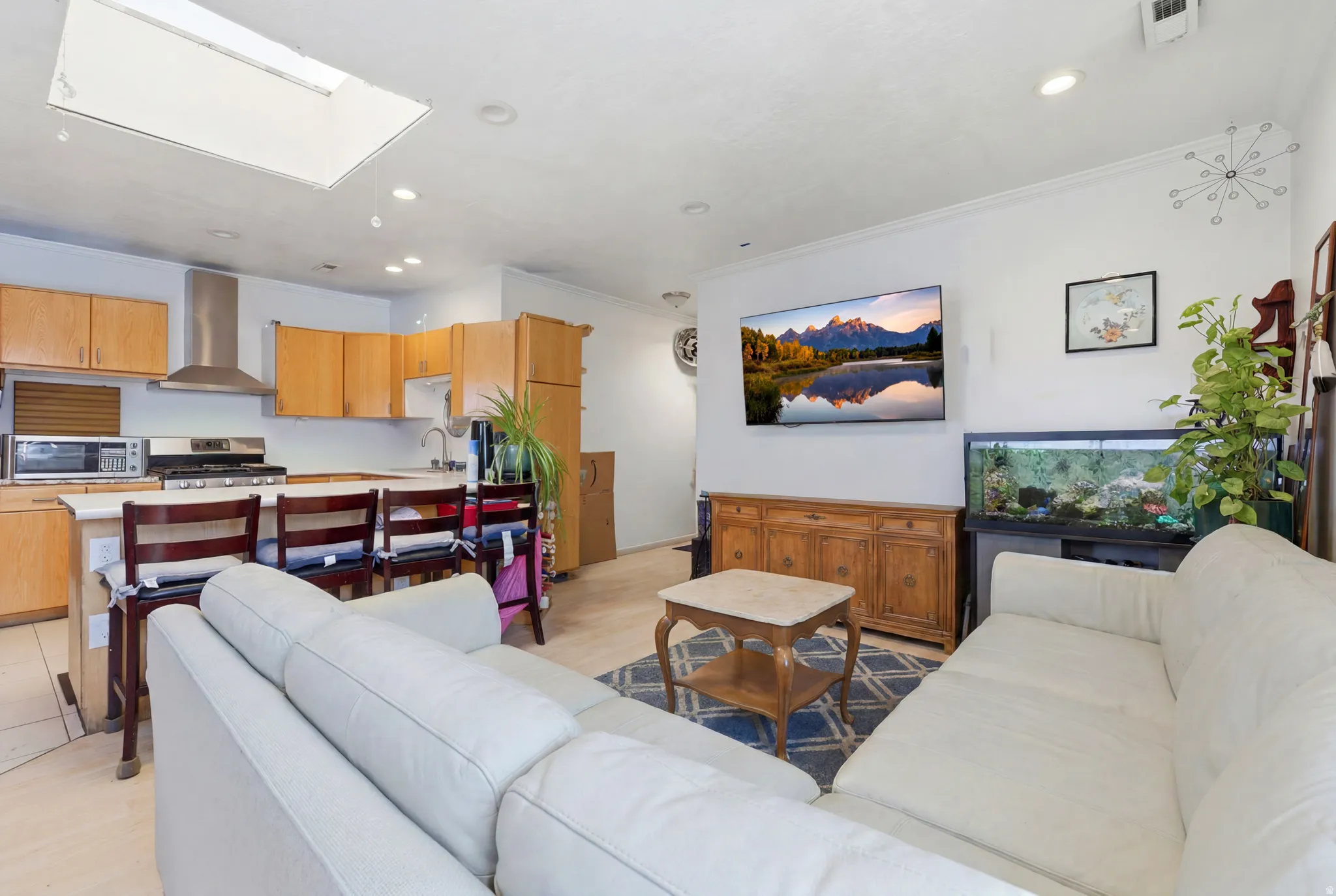 Open-concept living space featuring a kitchen with light wood cabinetry, white countertops, and stainless steel appliances