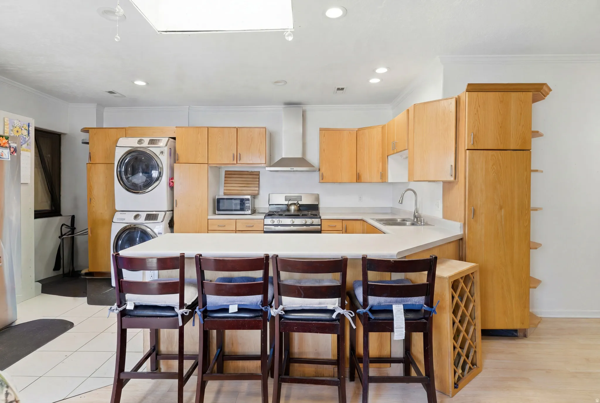 Open-concept kitchen featuring light wood cabinetry, white countertops, stainless steel appliances, a center island with seating, and a built-in wine rack