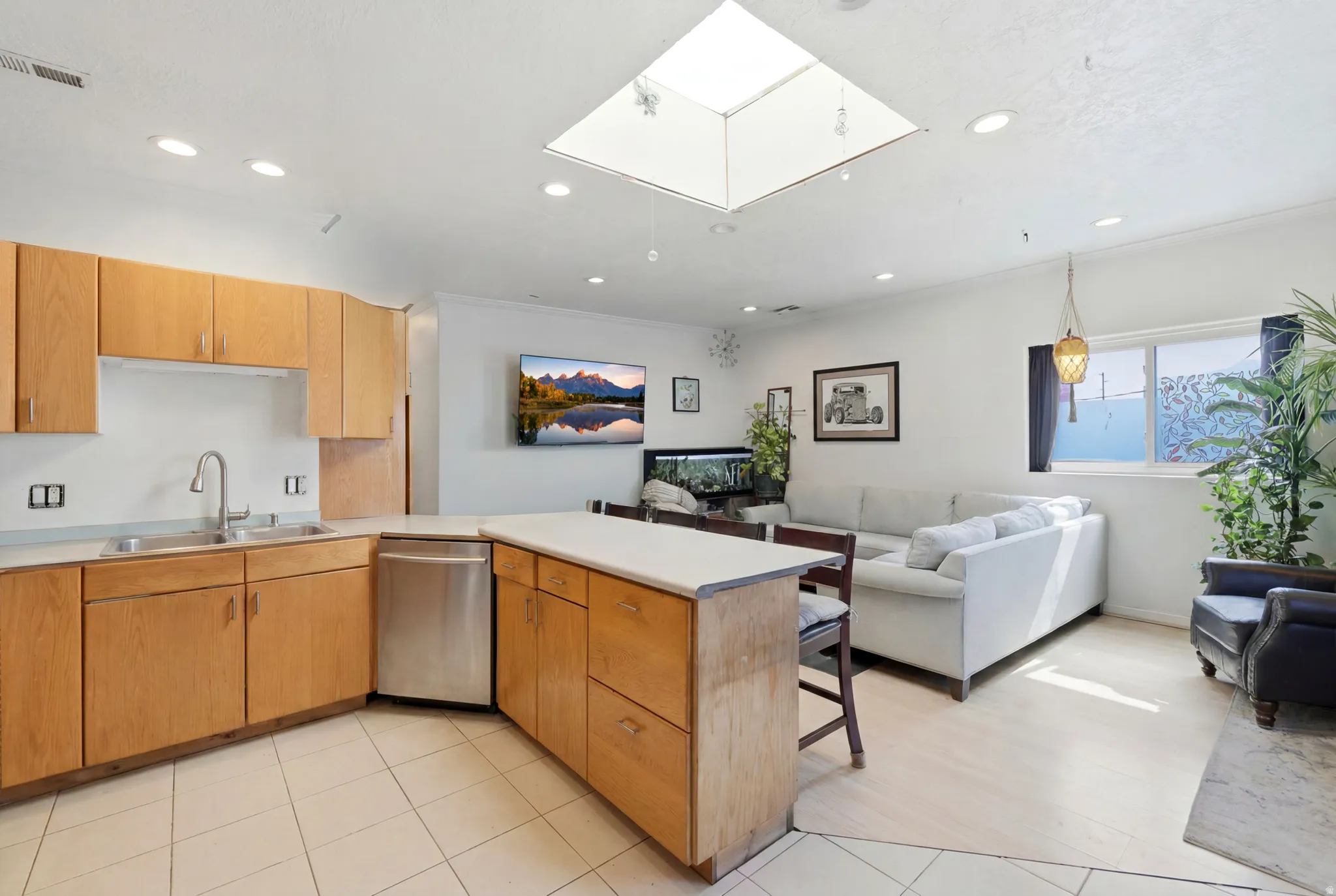 Open-concept living space featuring a skylight, recessed lighting, wood-finish cabinetry, stainless steel dishwasher, and a kitchen island with seating