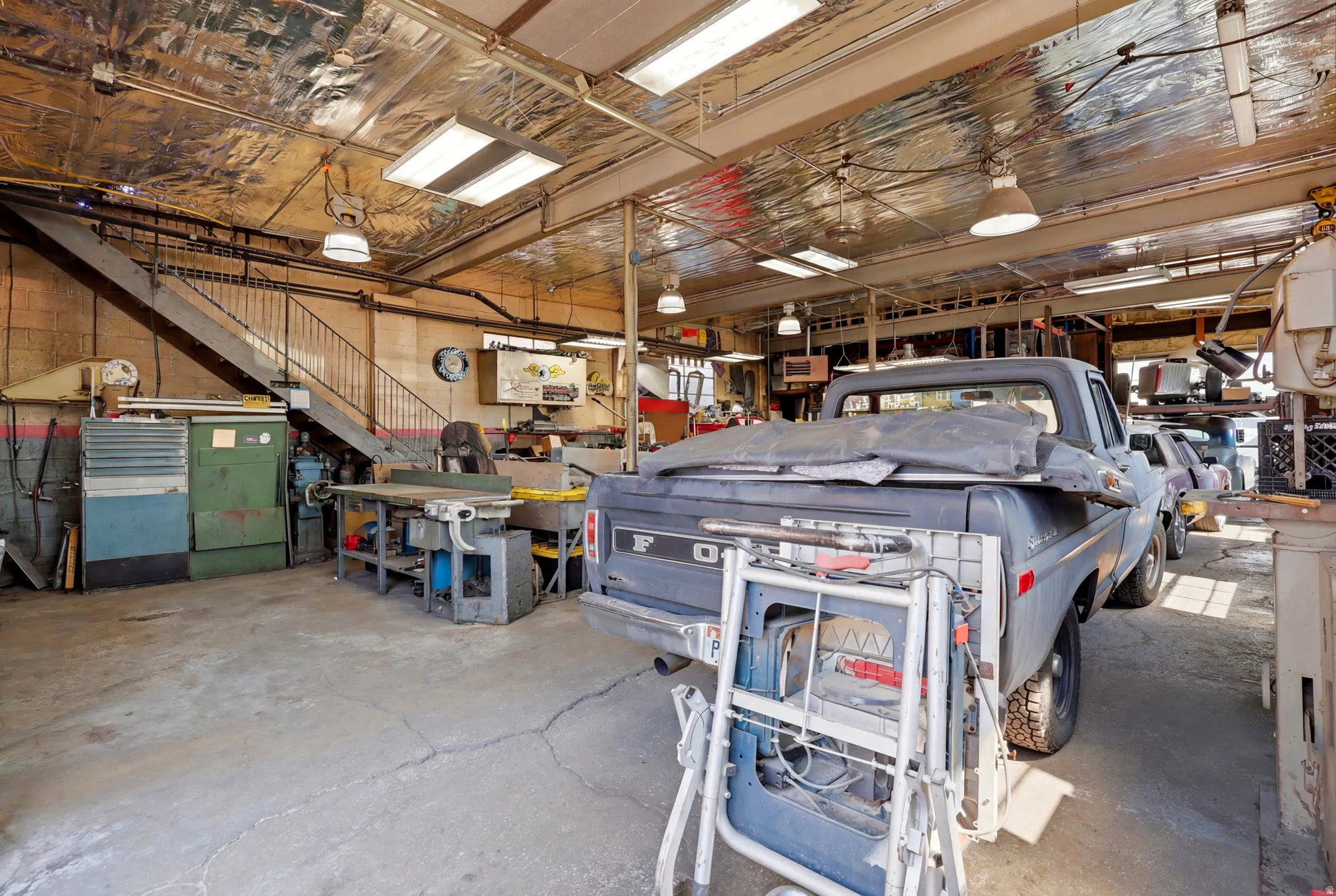 Spacious interior featuring a concrete floor, exposed metal ceiling with reflective insulation, and multiple fluorescent light fixtures