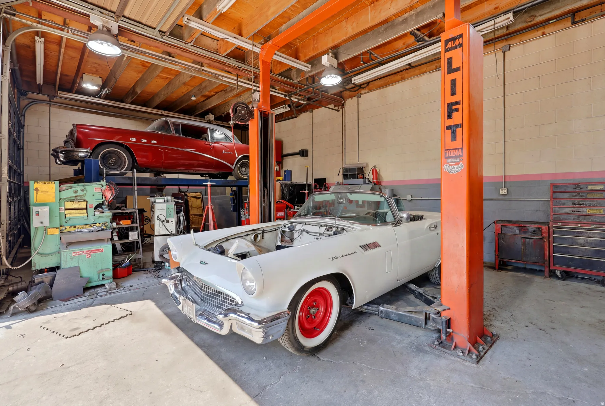 Spacious garage featuring a professional vehicle lift, exposed wood beam ceiling, concrete flooring, and built-in storage solutions