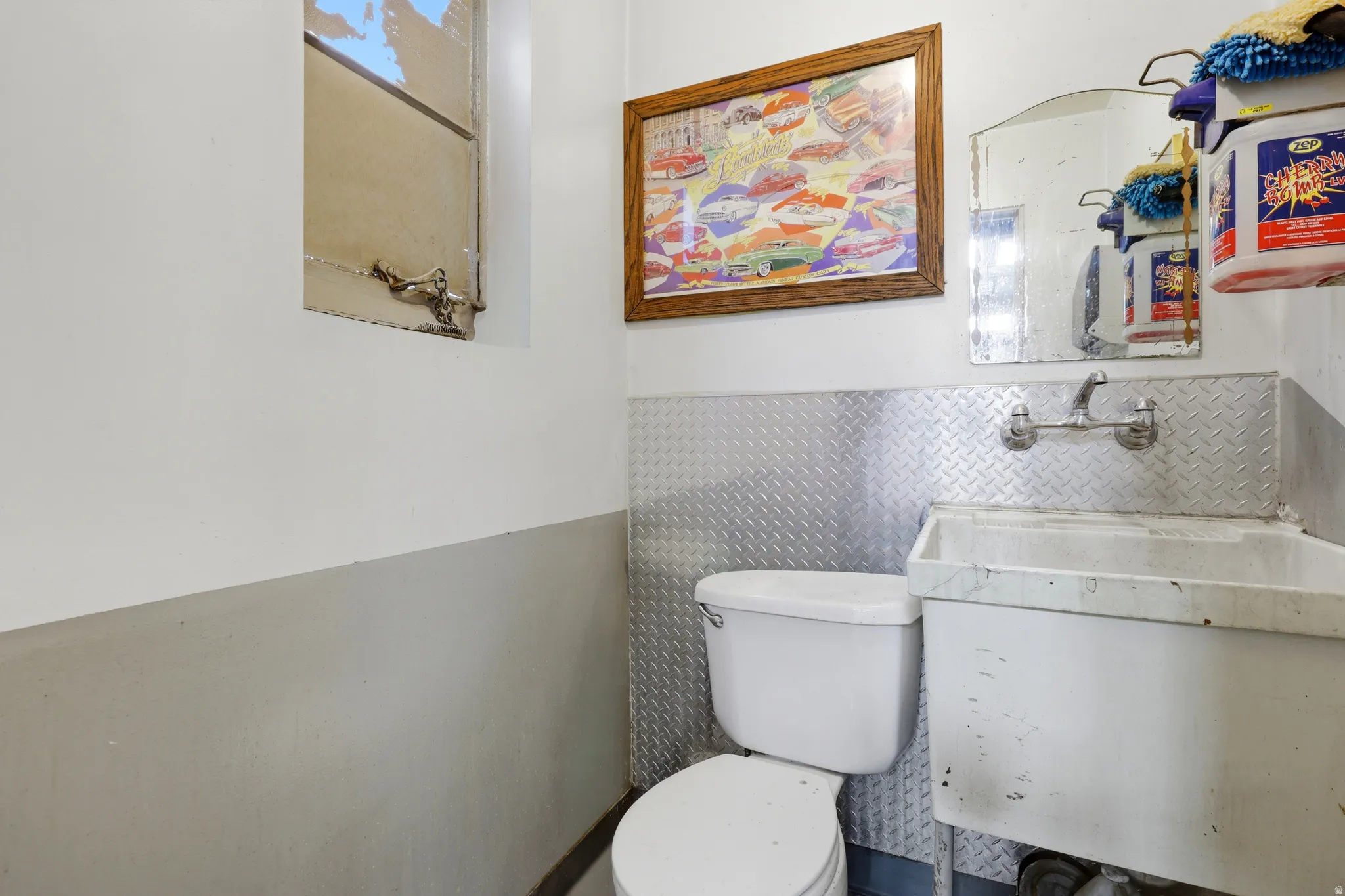Utility room featuring a white toilet, wall-mounted utility sink, and diamond plate wainscoting