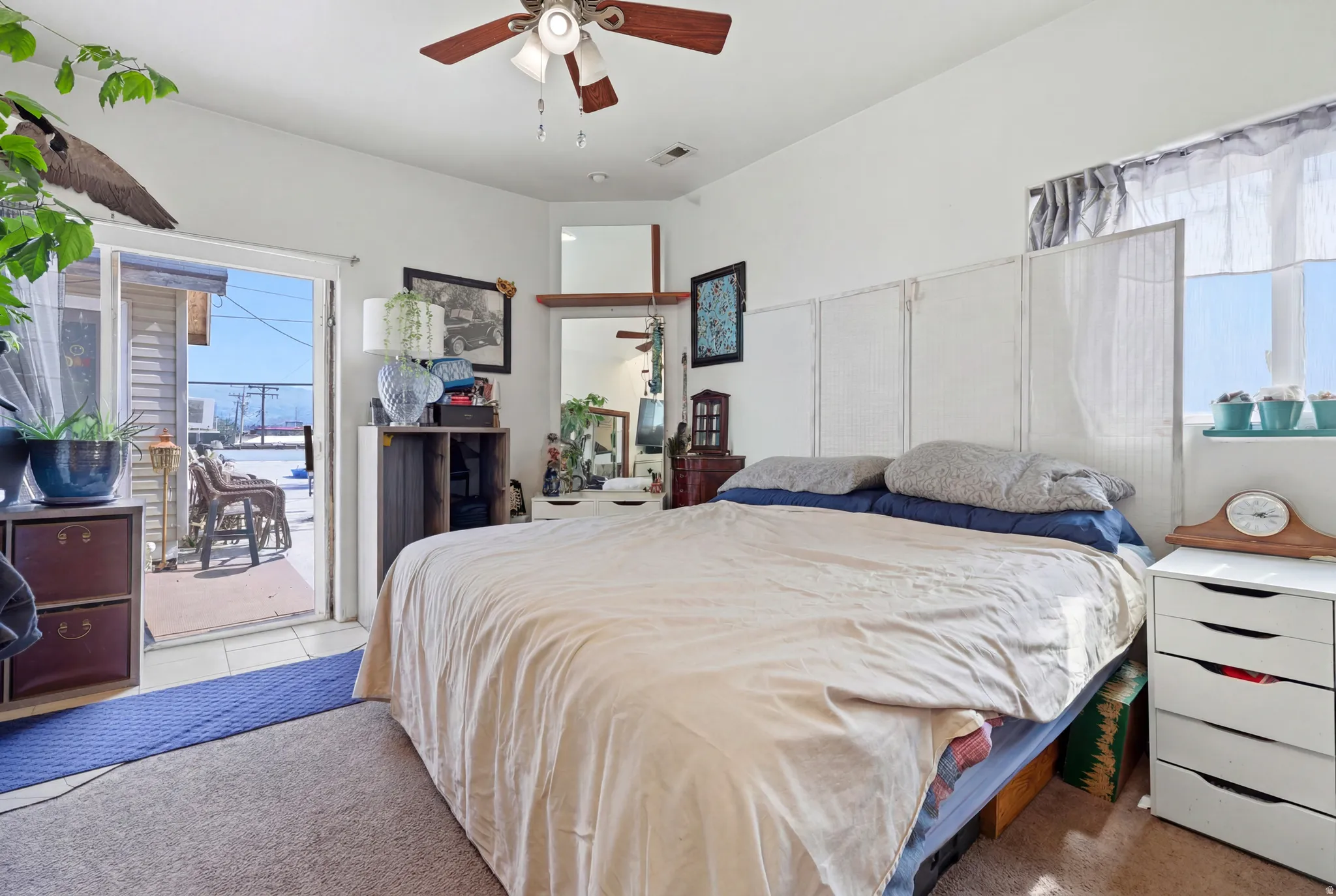 Carpeted interior space featuring a ceiling fan with integrated lighting, a corner vanity with a mirror, and a window with a sheer curtain