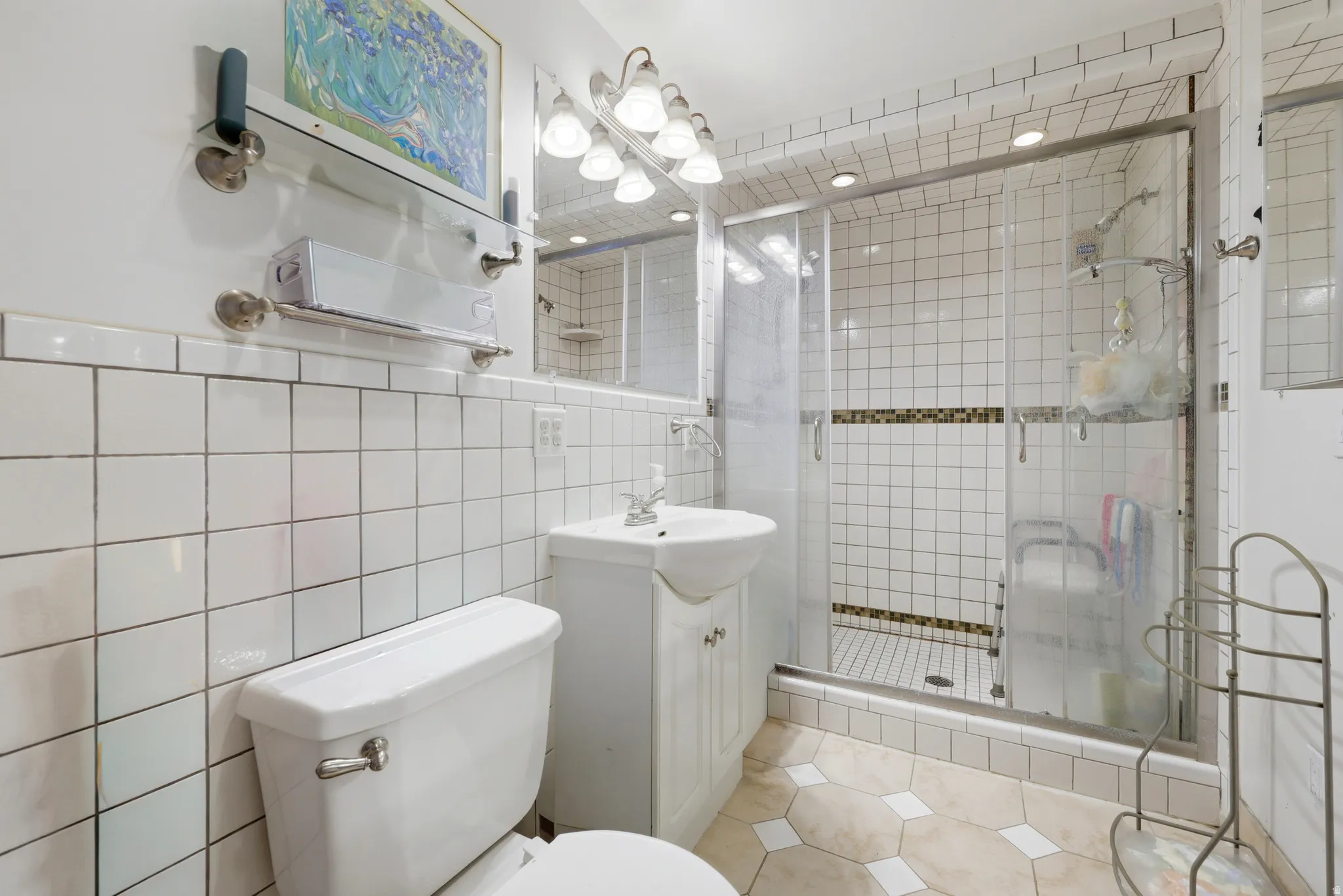 Tiled bathroom featuring a glass-enclosed shower with a mosaic accent band, a pedestal sink with vanity storage, and a built-in medicine cabinet