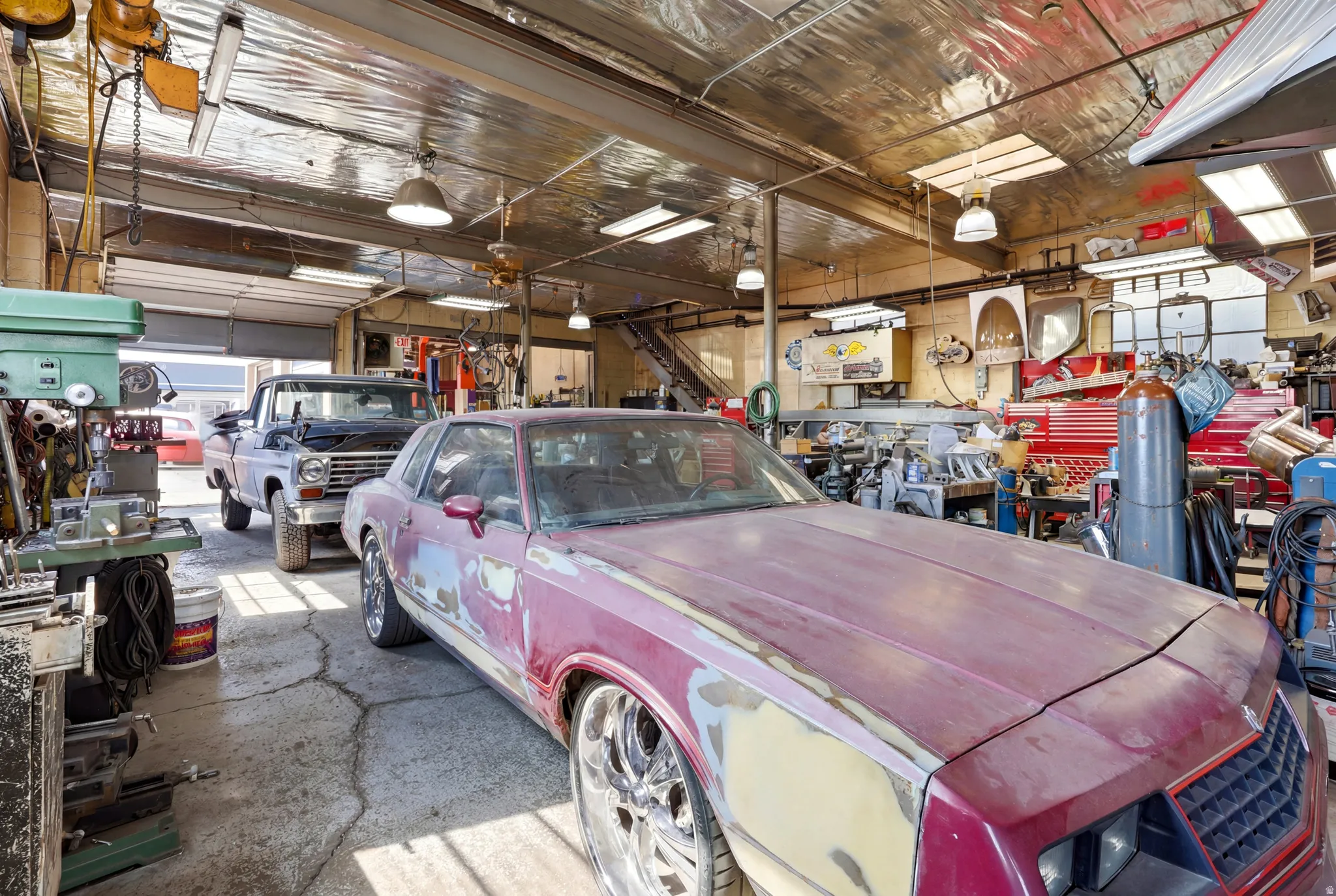 Spacious workshop featuring concrete flooring, multiple overhead garage doors, an insulated ceiling, fluorescent lighting, and skylights providing natural illumination