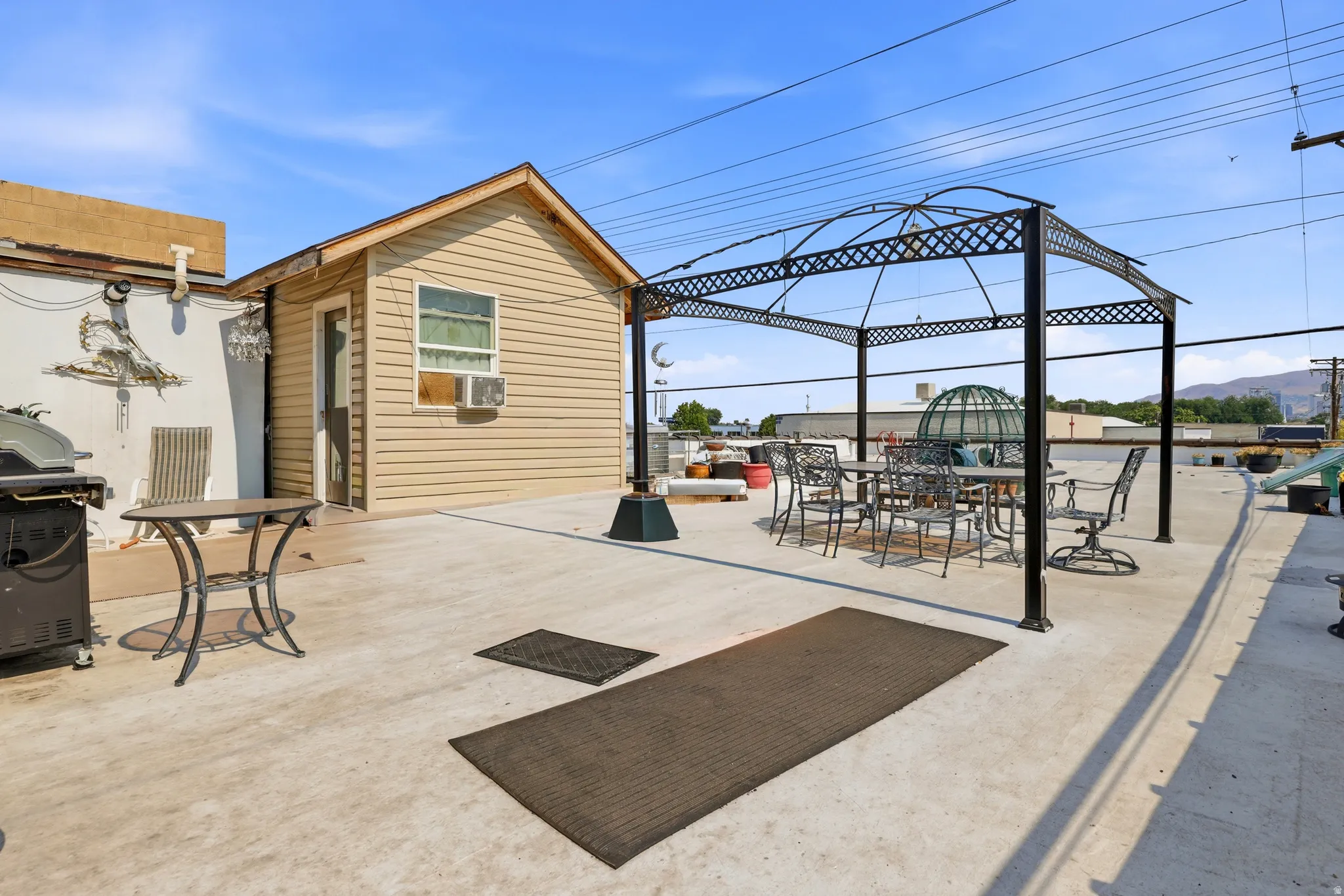 Rooftop patio featuring an outdoor gazebo structure, a beige siding shed with a window, and a concrete surface
