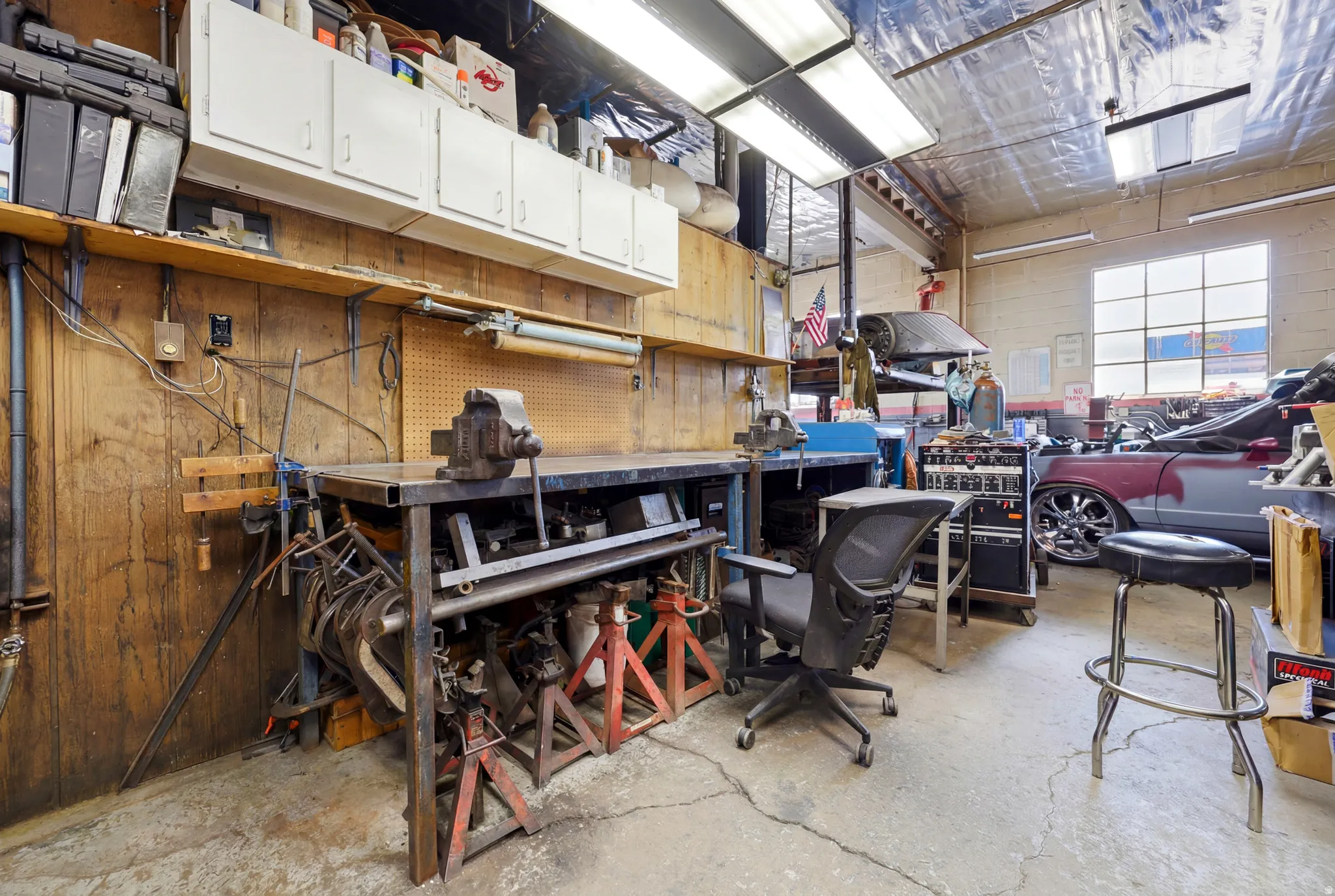 Spacious workshop area featuring concrete flooring, wood paneling, and an overhead storage cabinet system