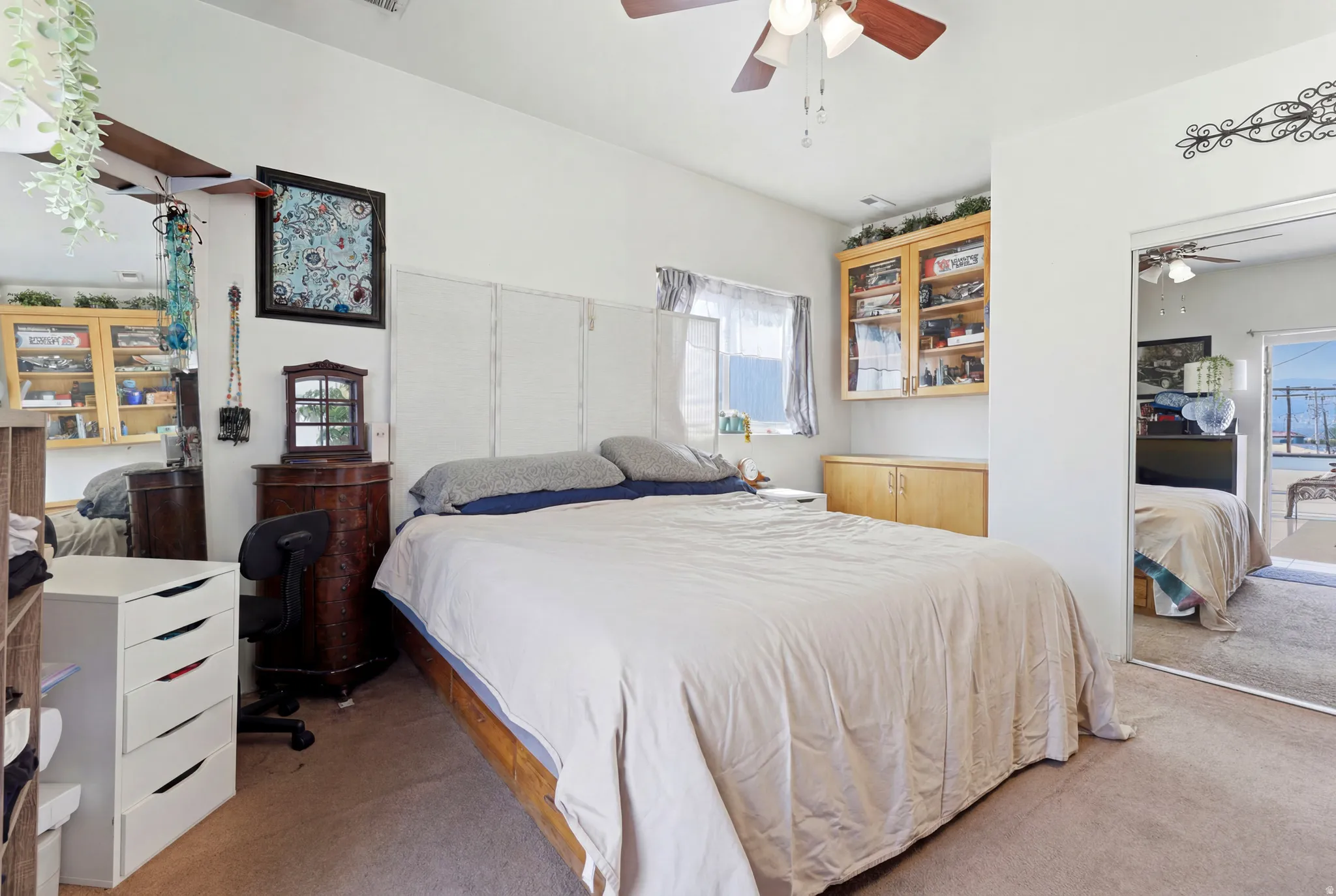 Bedroom featuring carpeted flooring, a ceiling fan with light fixture, built-in wooden cabinetry with glass-front uppers, and a mirrored closet door