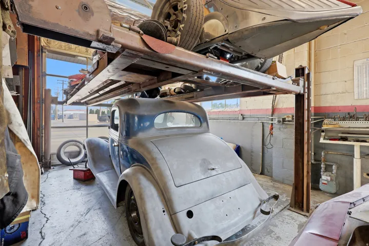 Automotive service bay featuring a hydraulic lift system, concrete flooring, exterior-facing windows, and block wall construction