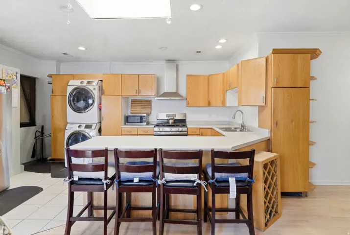 Open-concept kitchen featuring light wood cabinetry, white countertops, stainless steel appliances, a center island with seating, and a built-in wine rack