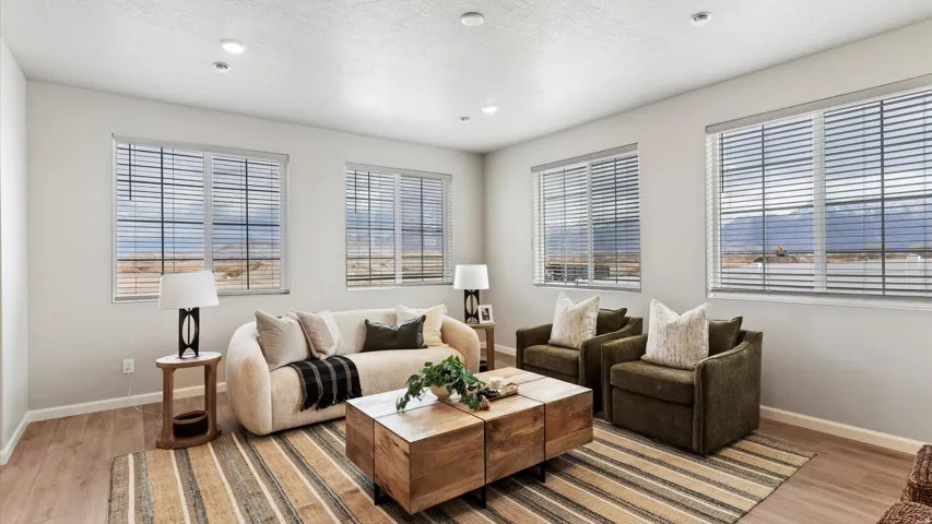 Spacious living area featuring light wood-finish flooring, recessed lighting, and multiple windows with horizontal blinds