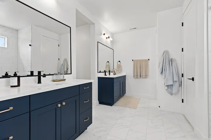 Dual navy blue vanities with white countertops, matte black fixtures, rectangular mirrors with black frames, and white tiled flooring