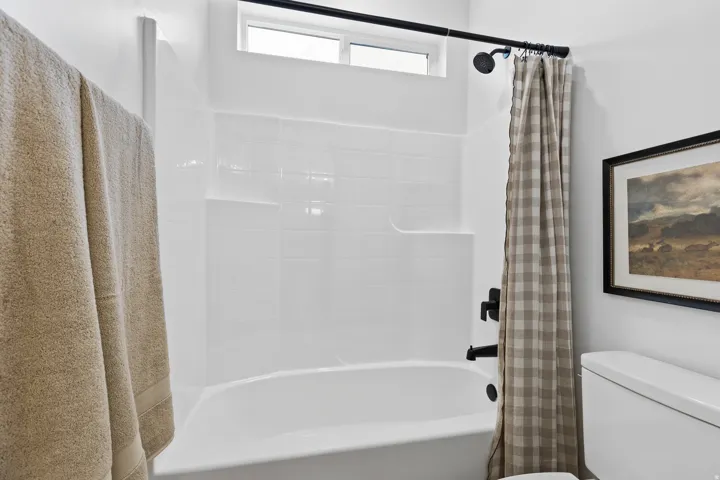 White bathtub and shower combination featuring a matte black shower head and faucet