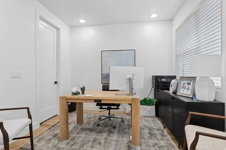 Dedicated room featuring recessed lighting, a window with horizontal blinds, wood-finish flooring, a solid core door with dark hardware, and a built-in storage cabinet