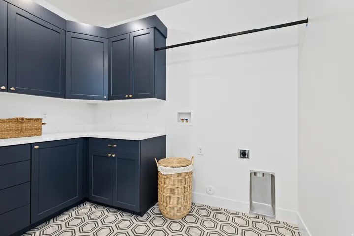 Laundry area featuring dark blue cabinetry with brass-finish hardware, white countertops, and a white subway tile backsplash