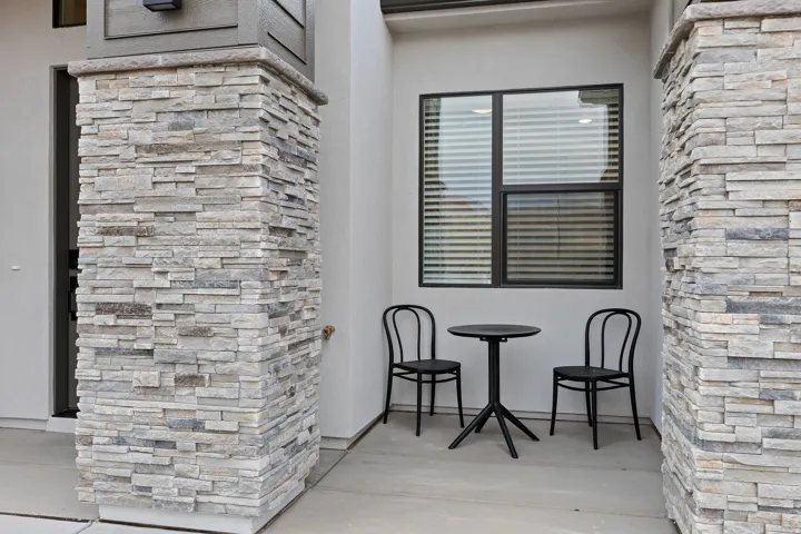 Exterior featuring stacked stone columns, a modern wall sconce, and dark-framed windows