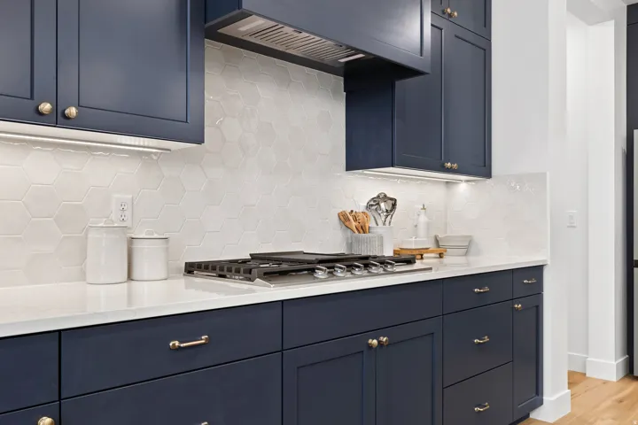 Kitchen featuring navy cabinetry, white countertop, hexagon tile backsplash, and a built-in gas range with a stainless steel hood