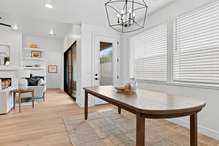 Bright dining area featuring wood-finish flooring, a contemporary chandelier, multiple windows with blinds, a glass-paneled door, and an open concept to a living space with built-in shelving