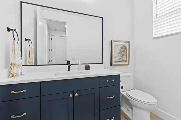 Bathroom featuring a dark blue vanity with gold-tone hardware, a white countertop with integrated sink, and a large mirror with a black frame