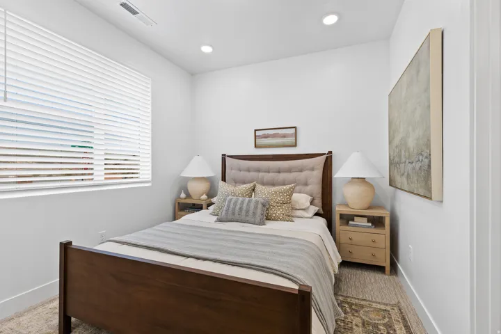Bright bedroom featuring a large window with horizontal blinds, recessed ceiling lighting, and light-toned walls