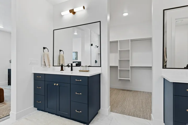 Bathroom vanity featuring a dark blue cabinet with brass hardware, a white countertop, and a rectangular mirror with a black frame