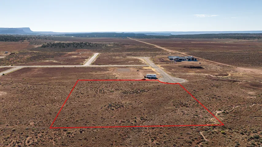 Expansive undeveloped lot featuring a distinct property boundary, visible road access, and distant mesa formations