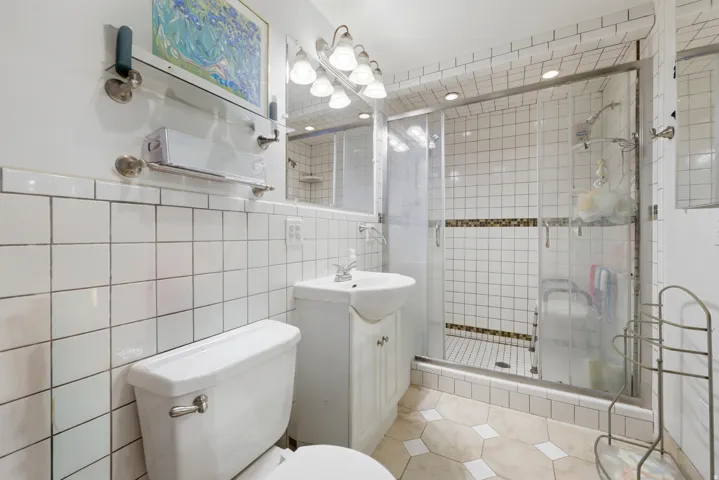 Tiled bathroom featuring a glass-enclosed shower with a mosaic accent band, a pedestal sink with vanity storage, and a built-in medicine cabinet