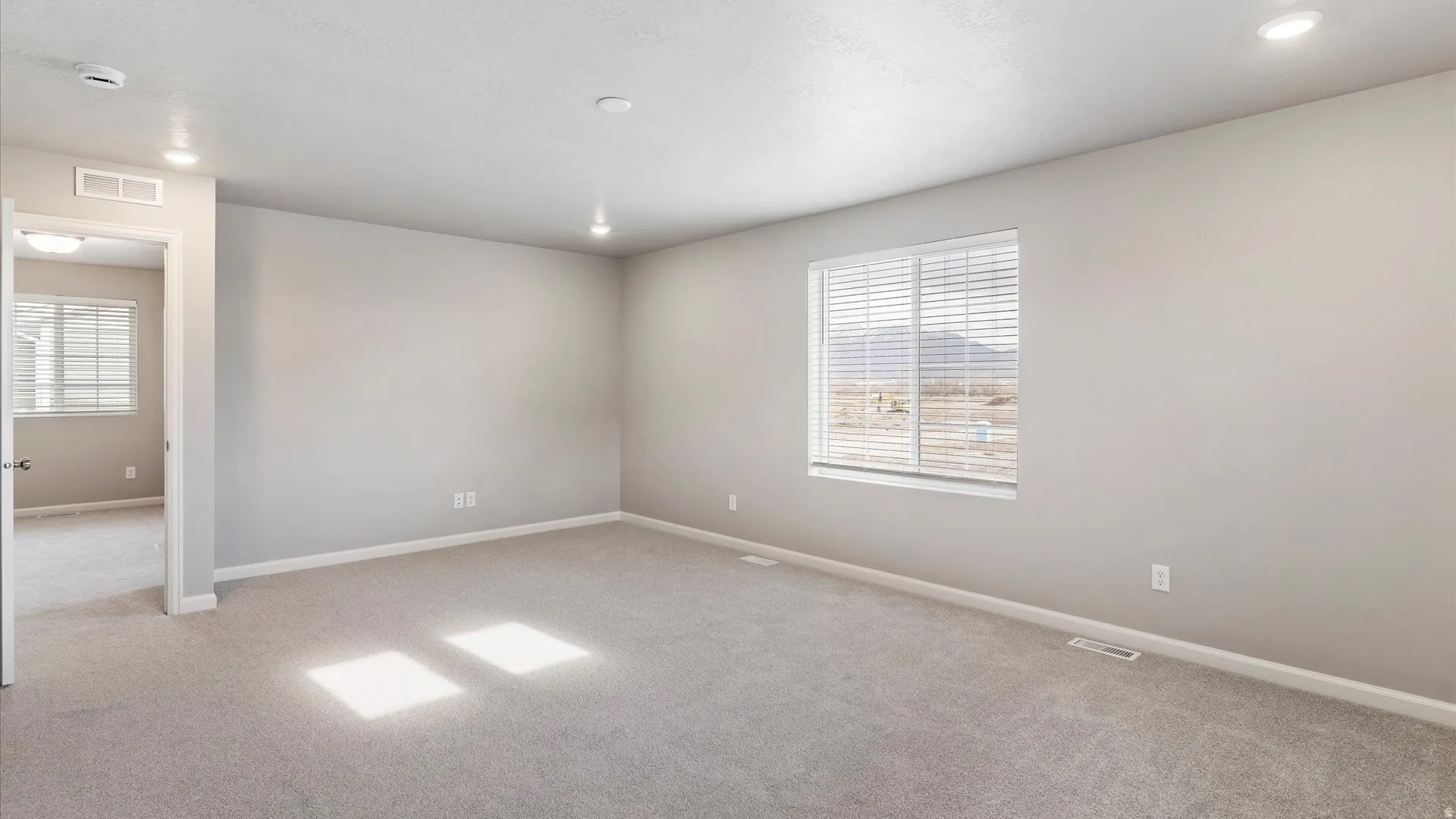 Spacious carpeted room with neutral paint, recessed lighting, and a window with horizontal blinds