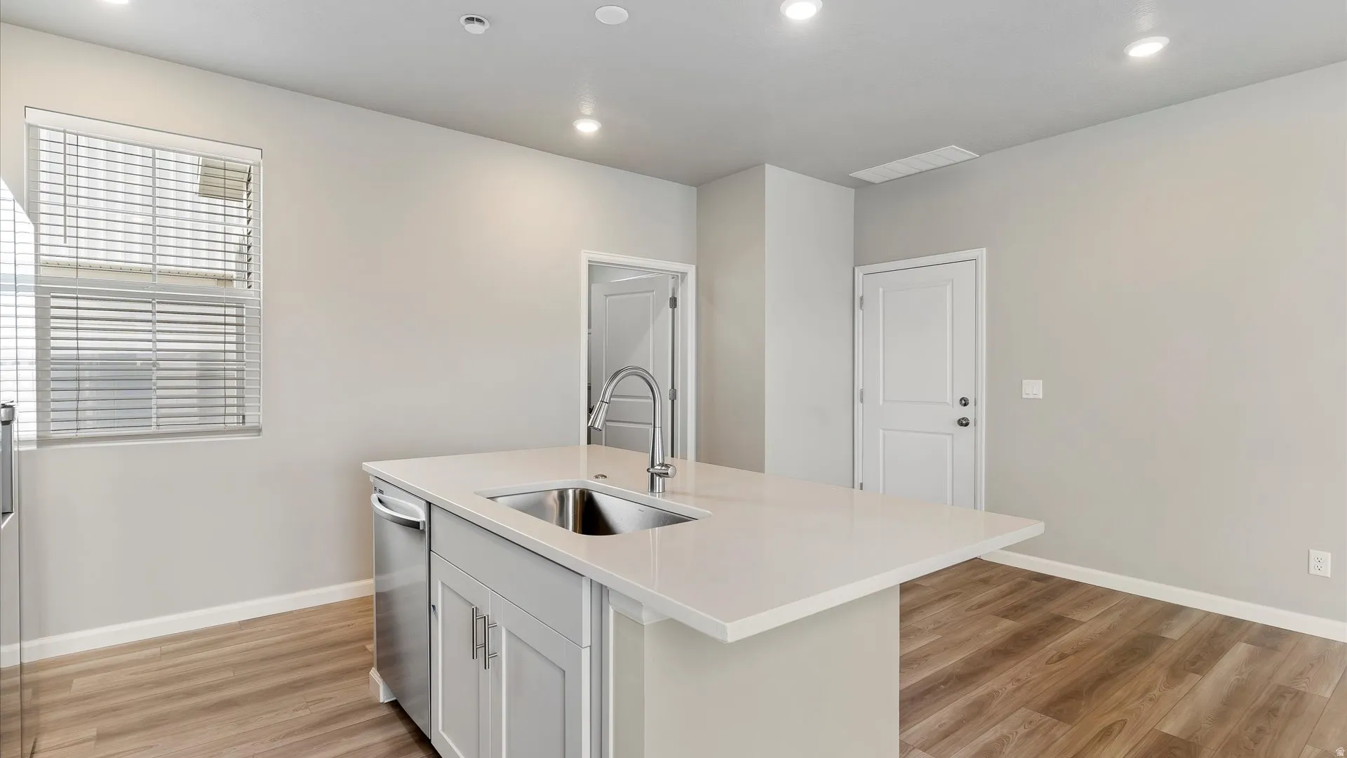 Kitchen island featuring a stainless steel sink with a high-arc faucet, light gray cabinetry, and a white countertop