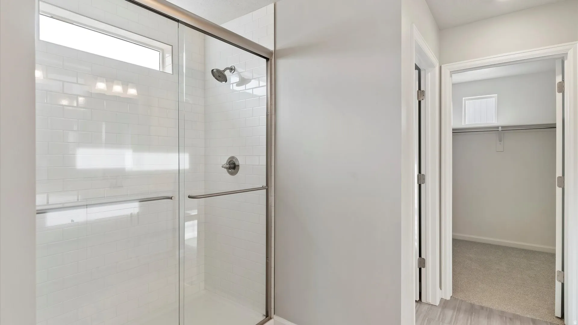 Shower with subway tile surround, glass enclosure, brushed nickel fixtures, and transom window