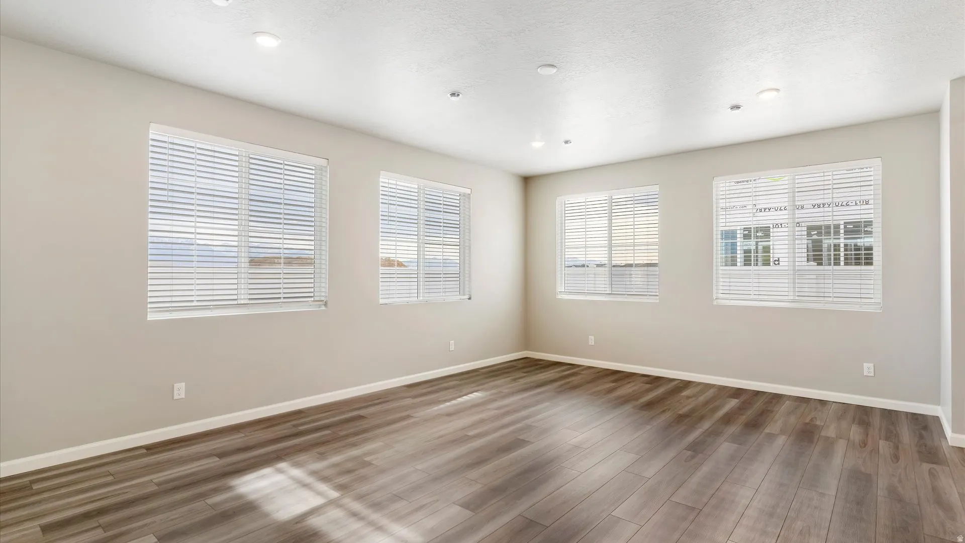 Spacious room featuring wood-finish flooring, light grey walls, white trim, and multiple windows with horizontal blinds