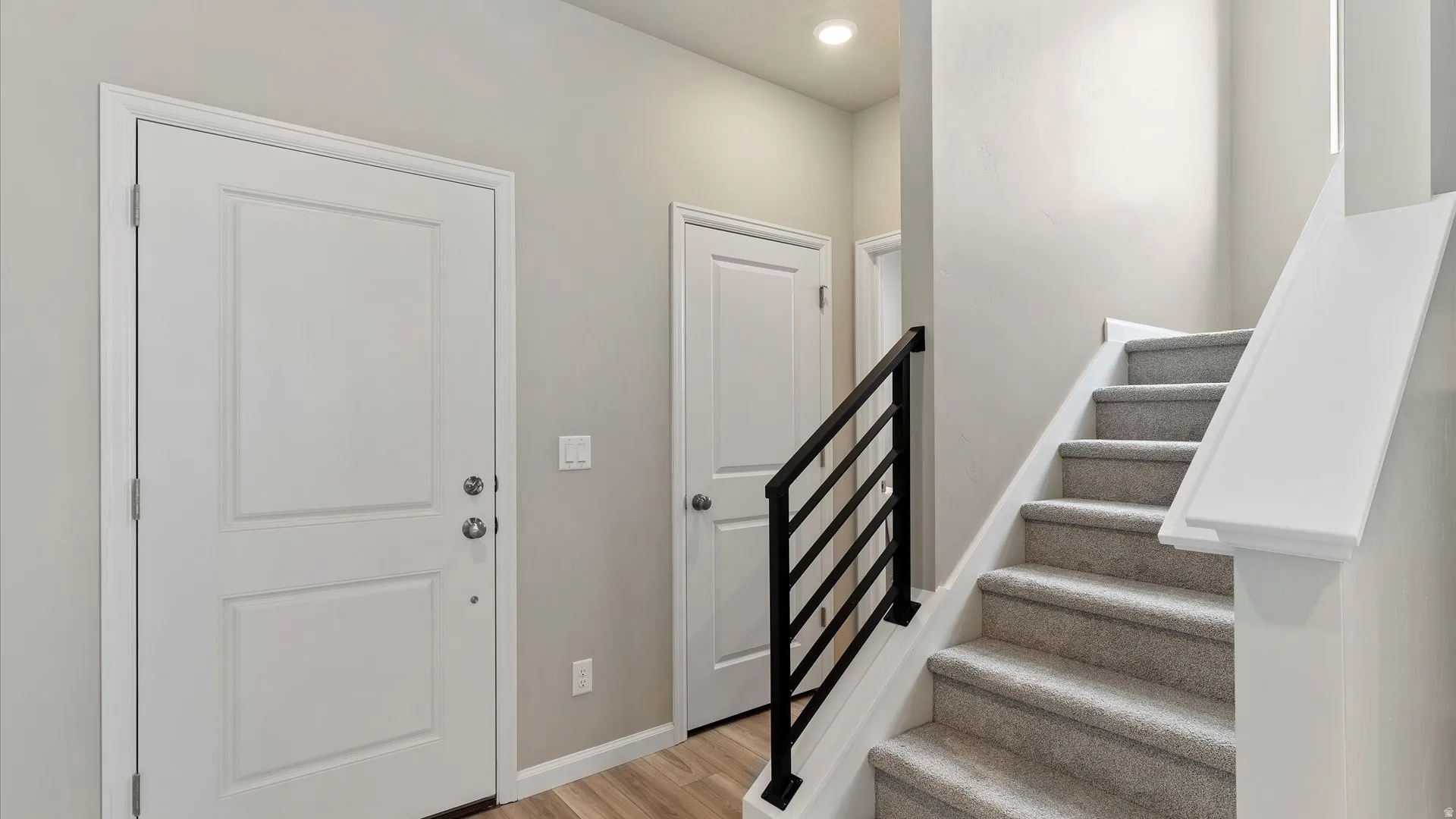 Carpeted staircase featuring a modern black metal railing, white risers, and a prominent white newel post