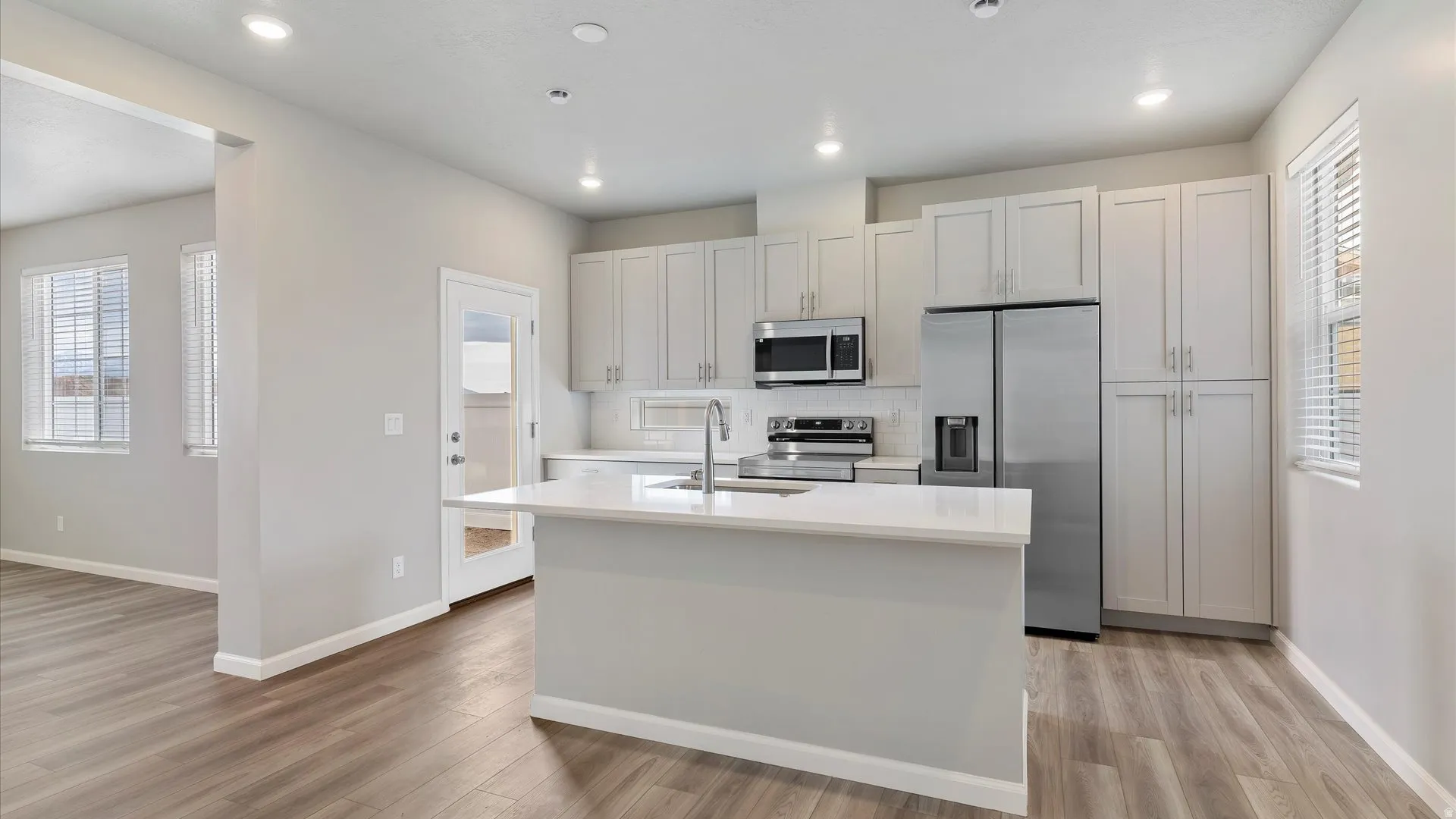 Contemporary kitchen featuring an island with a breakfast bar, light-toned cabinetry, stainless steel appliances, and wood-finish flooring