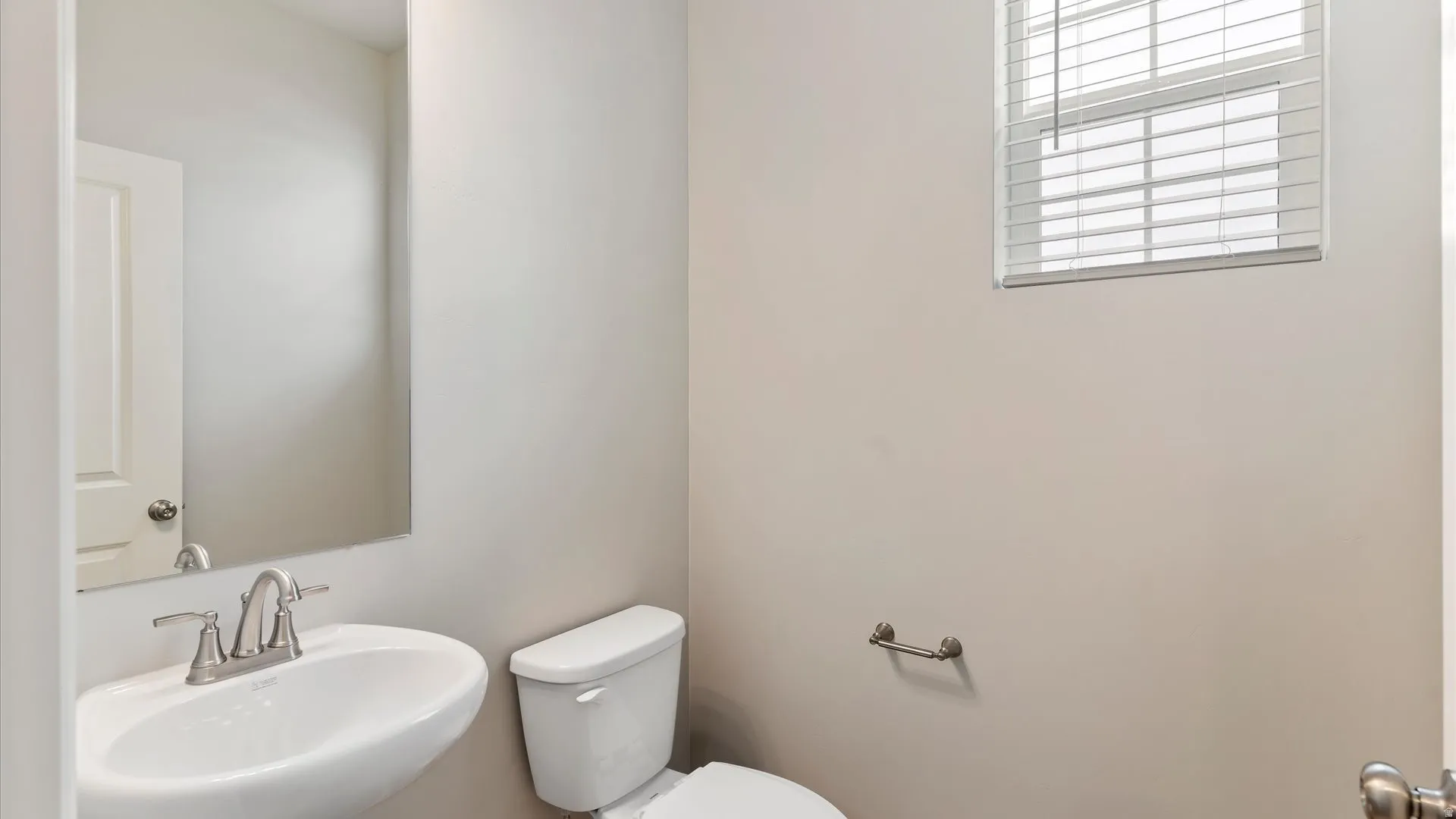 Powder room featuring a pedestal sink with a brushed nickel faucet, a white toilet, and a window with horizontal blinds