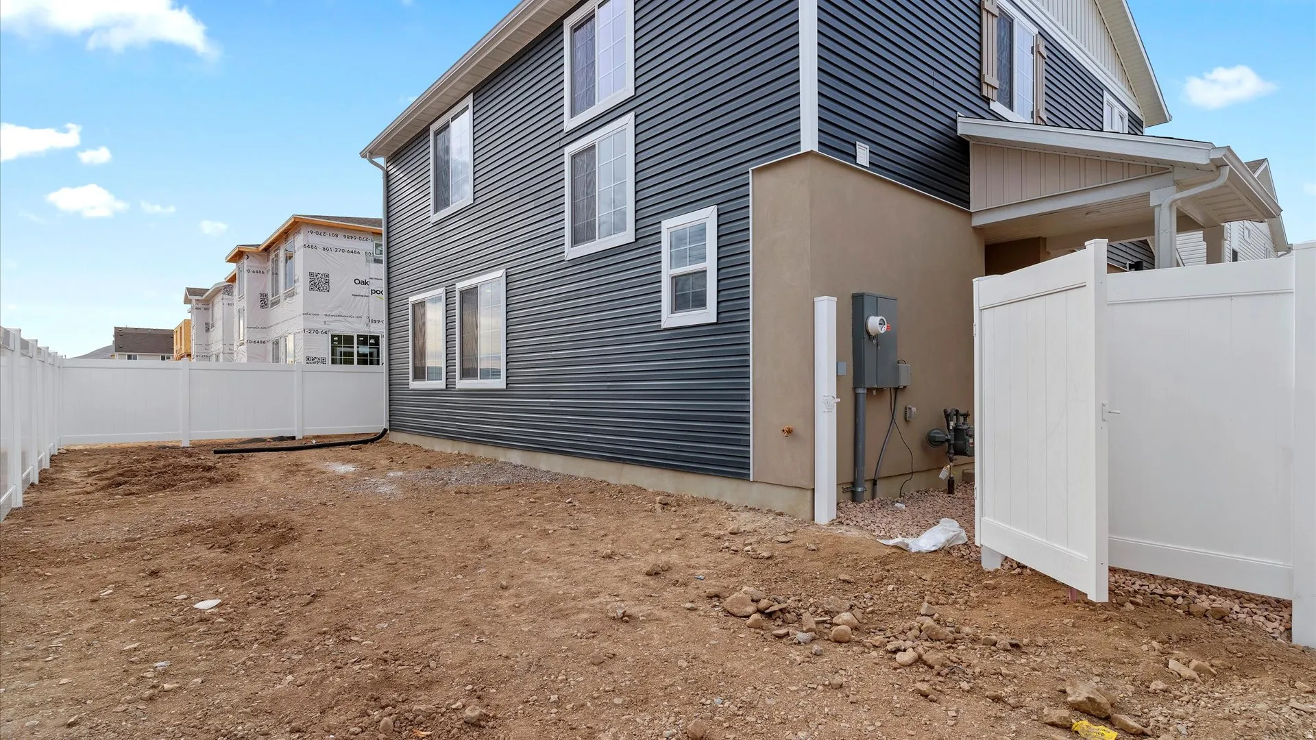 Side exterior featuring dark gray horizontal siding, white trim windows, and a partially fenced yard