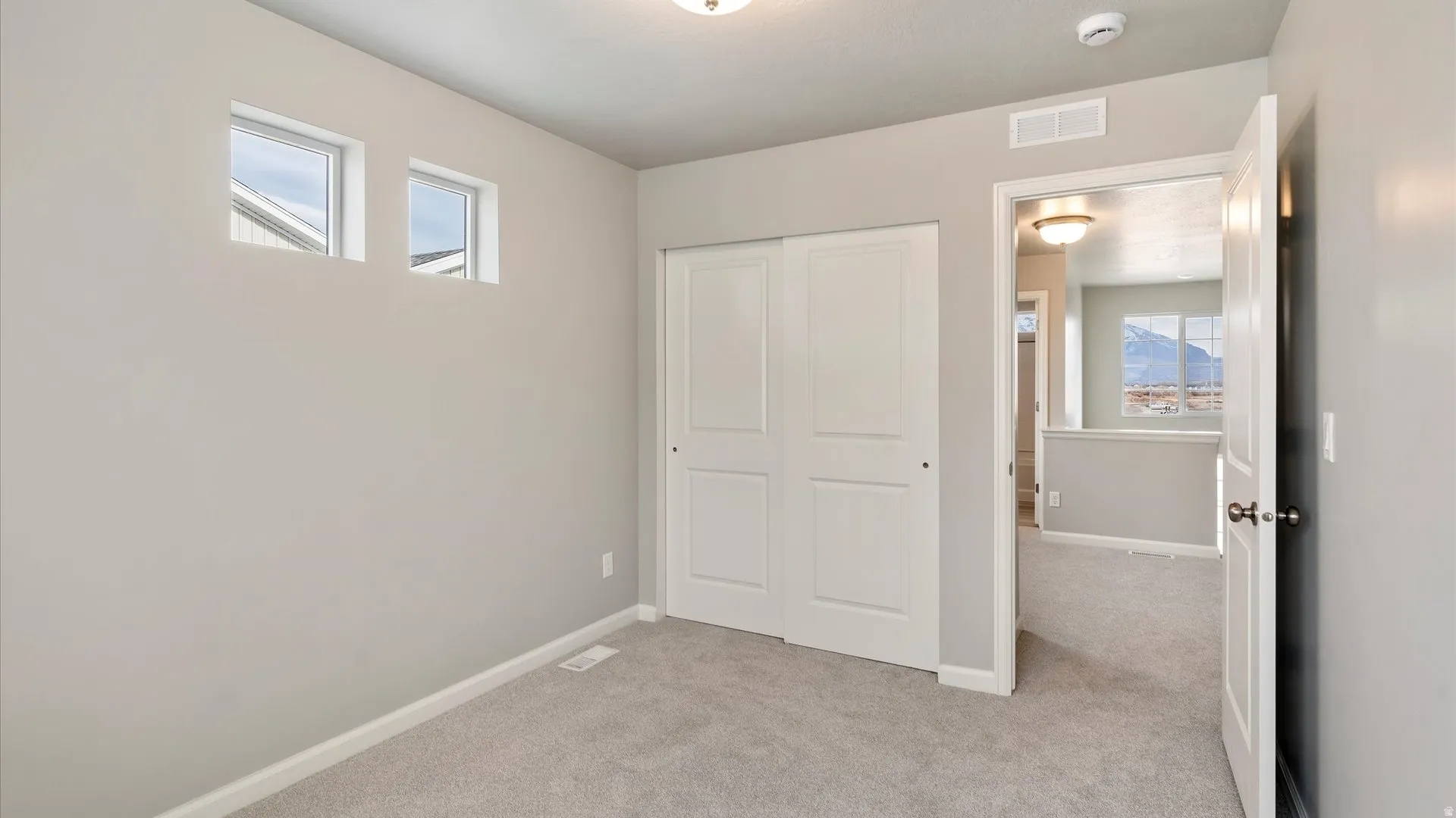 Carpeted room with a double-panel sliding closet door, white baseboards, and two transom windows