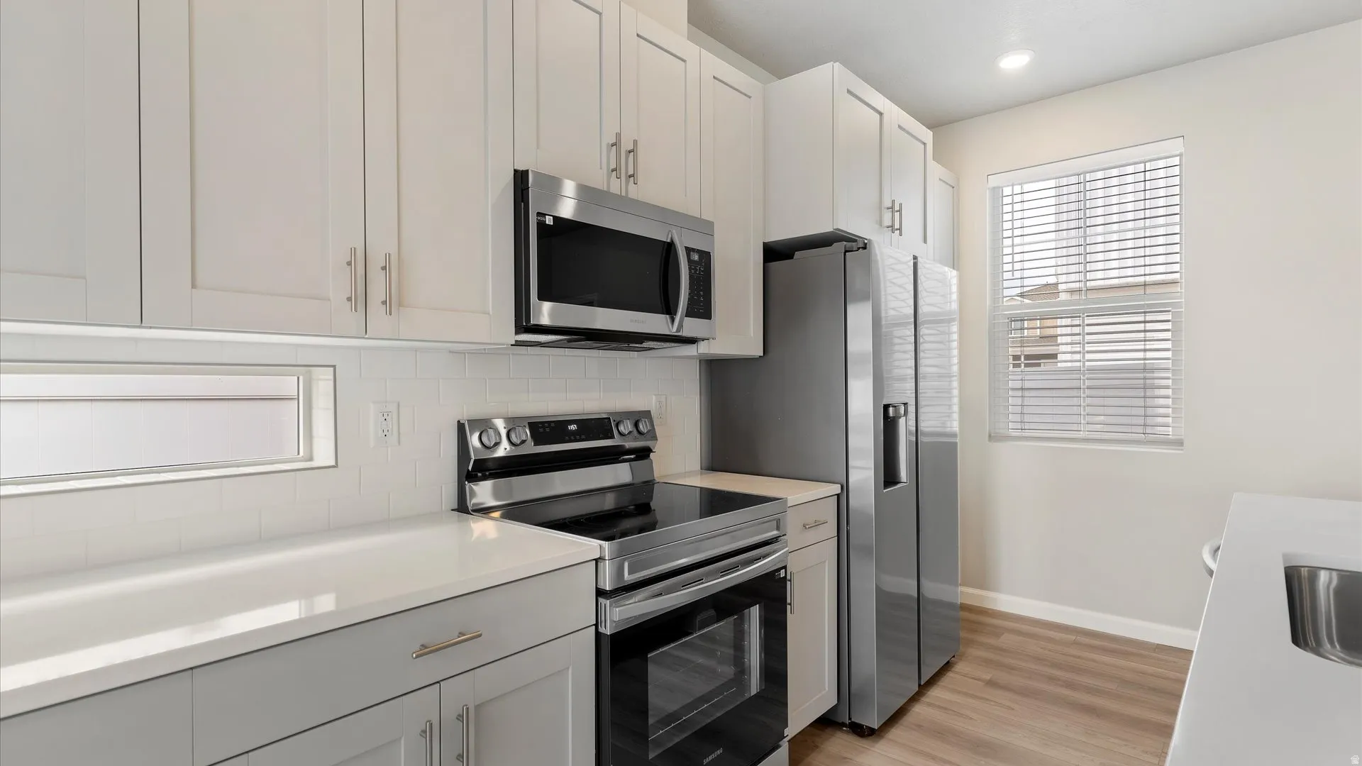 Modern kitchen featuring white shaker cabinetry, stainless steel appliances, white subway tile backsplash, and light wood-finish flooring
