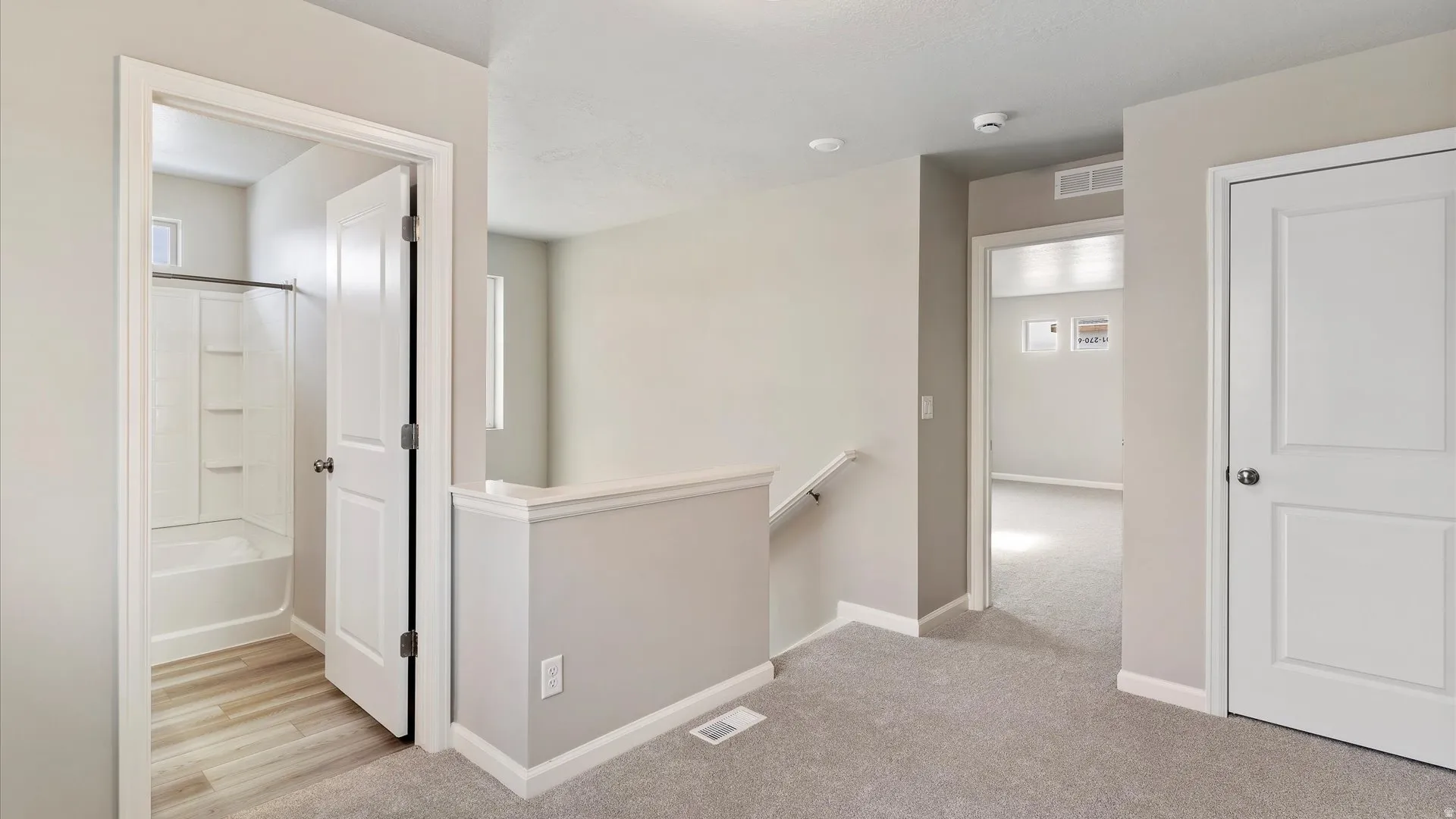 Upper-level landing featuring light gray carpeting and a white painted handrail