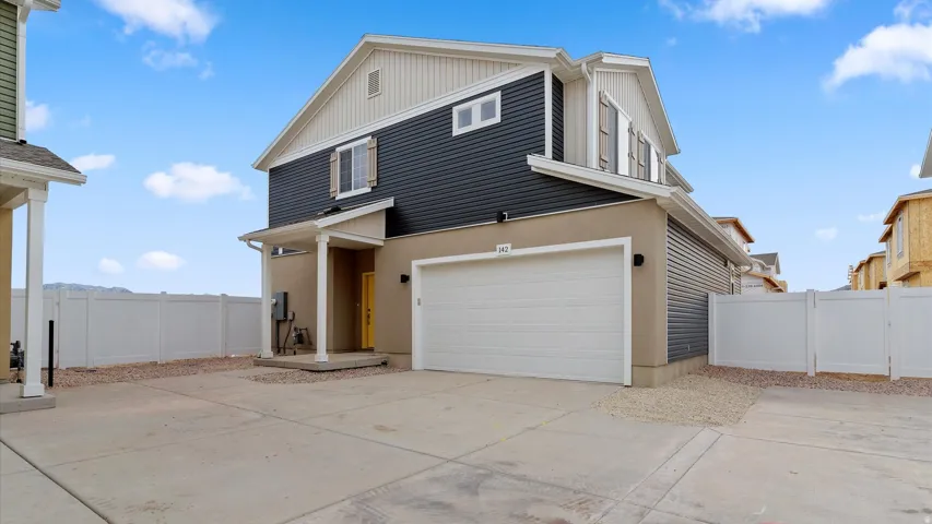 Two-story stucco and siding exterior featuring a prominent garage, covered porch entry, and a contrasting yellow front door