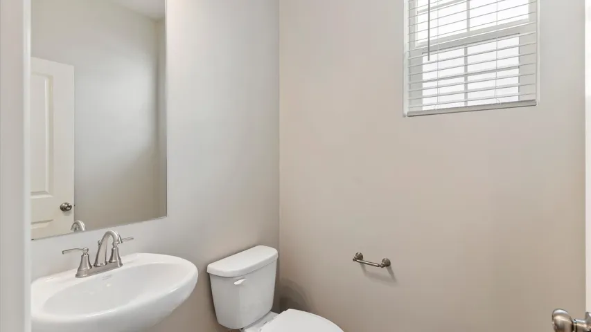 Powder room featuring a pedestal sink with a brushed nickel faucet, a white toilet, and a window with horizontal blinds