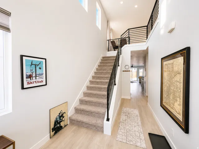 Two-story entry featuring light wood-finish flooring, a carpeted staircase with modern black horizontal metal railings, and a second-story landing