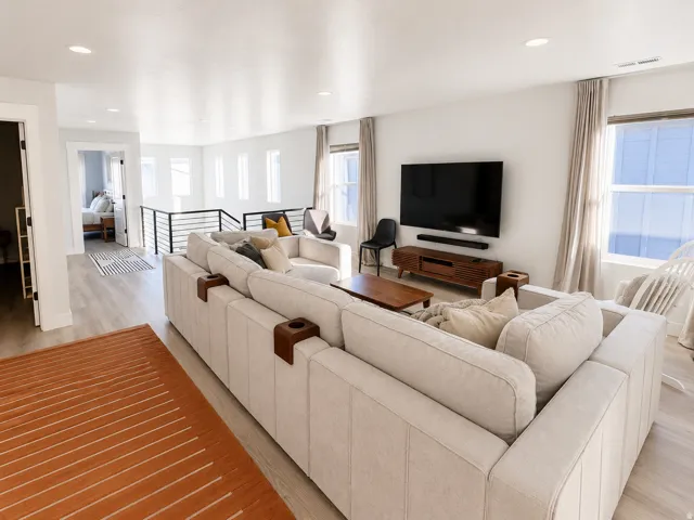 Spacious upper-level area featuring light wood-finish flooring, recessed lighting, and a modern horizontal railing