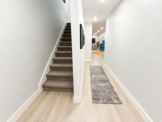 Carpeted staircase alongside a hallway with wood-finish flooring, recessed lighting, and crisp white baseboards