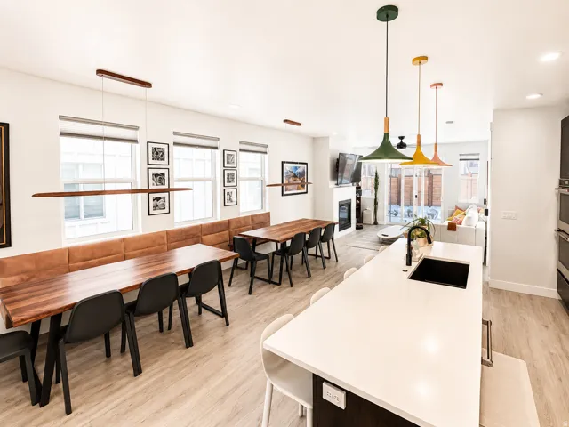 Open-concept living space featuring wood-finish flooring, a contemporary kitchen island with an undermount sink, and integrated dining banquettes