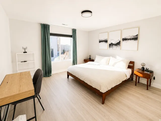 Spacious bedroom featuring light wood-finish flooring, a large window with privacy curtains, recessed lighting, and ample wall space