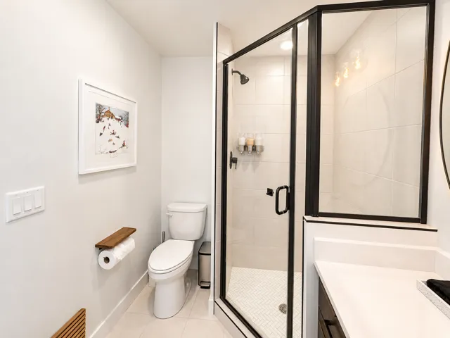 Contemporary bathroom featuring a glass-enclosed shower with black framing, white subway tile walls, and a white herringbone tile floor