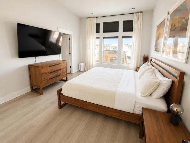 Spacious bedroom featuring light wood-finish flooring and expansive windows with roller shades