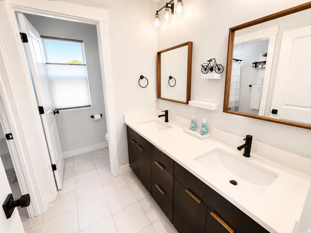 Double vanity featuring integrated sinks, white countertops, dark wood-finish cabinetry with gold-tone hardware, and matte black fixtures