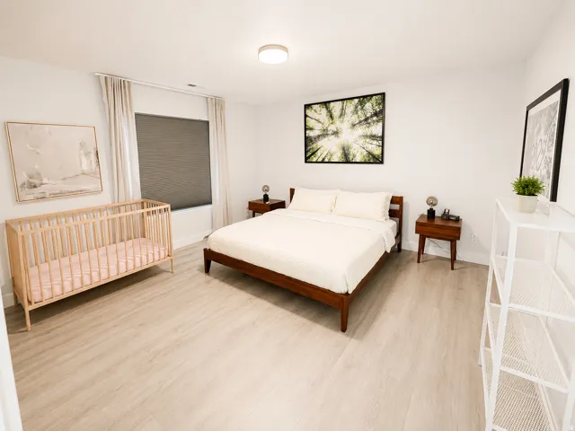Spacious bedroom featuring light wood-finish flooring, white walls, and a window with blinds and drapes