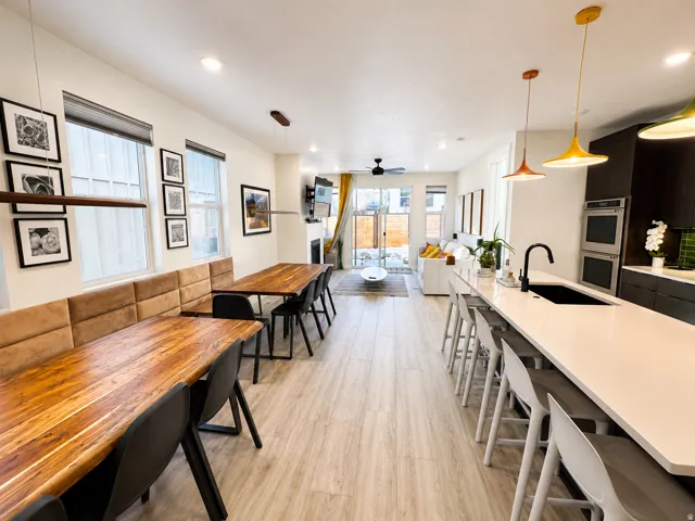 Expansive open-concept living space featuring wood-finish flooring, a contemporary kitchen island with a built-in sink and seating, integrated double ovens, and a dining area with built-in bench seating
